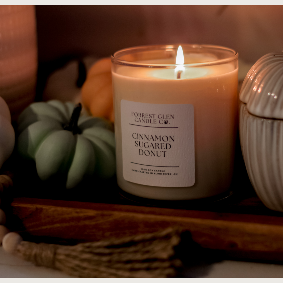 lit soy wax candle in the fragrance 'cinnamon sugared donut'on wooden decor tray with fall decor around it. including decor pumpkinspumpkins