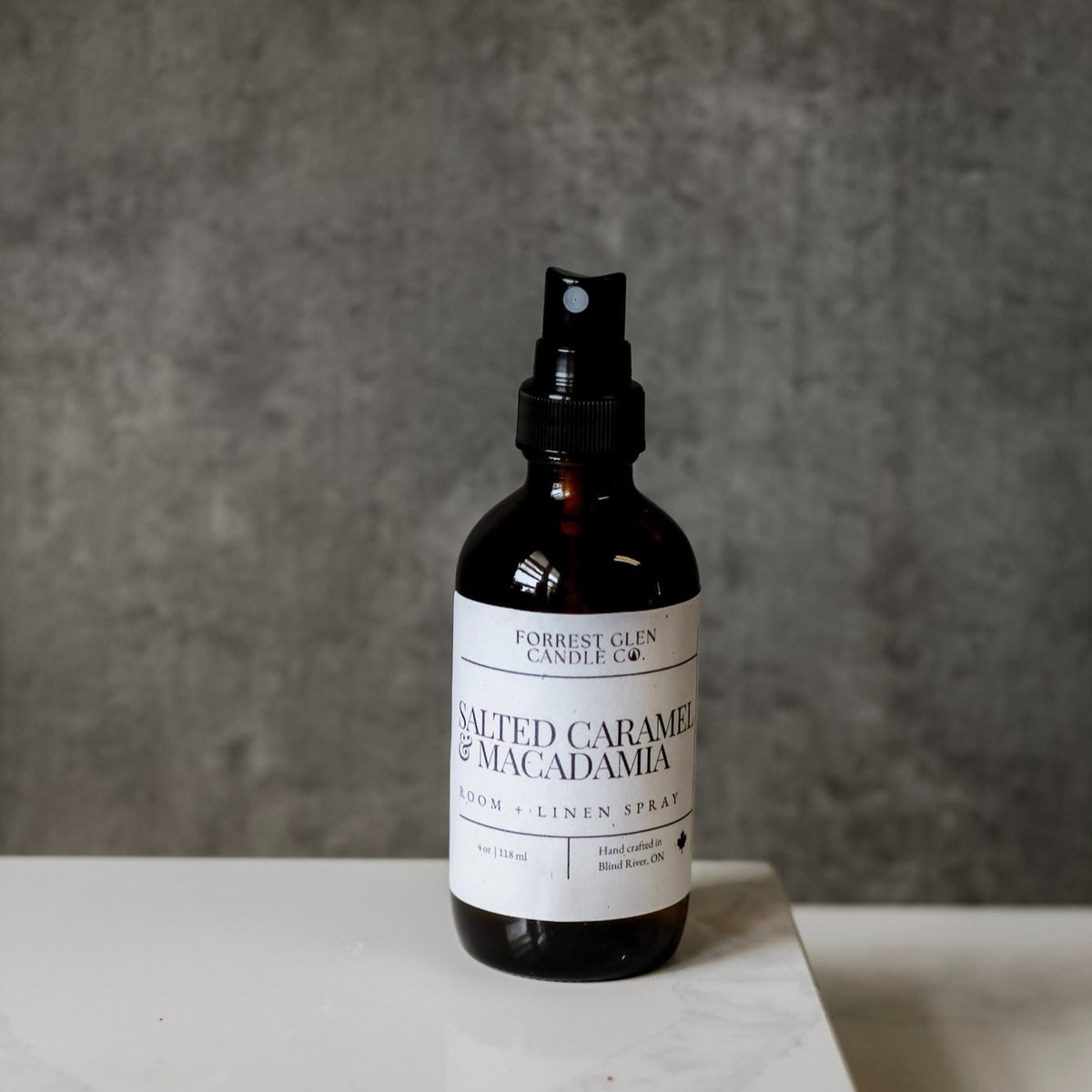 Bottle of 'Salted Caramel & Macadamia' room spray on a gray surface with a neutral background