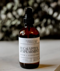 Bottle of Eucalyptus & Spearmint room and linen spray on a surface with a blurred  eucalyptus background