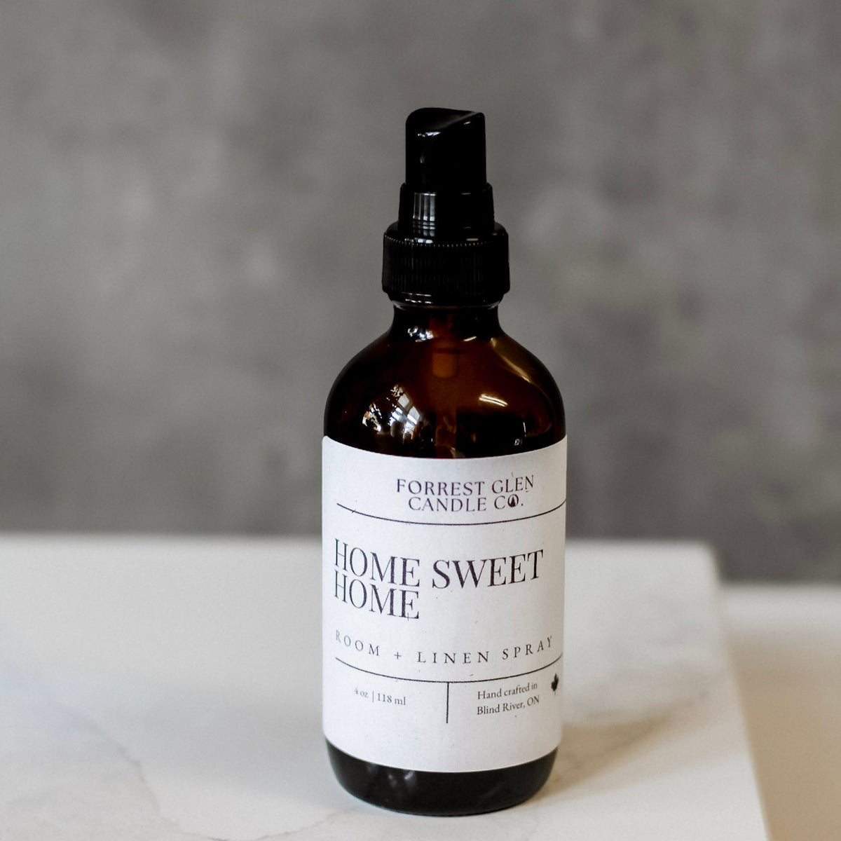 Bottle of 'Home Sweet Home' room and linen spray on a white surface with a gray background
