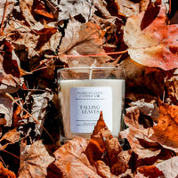 Candle labeled 'Falling Leaves' surrounded by autumn leaves