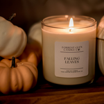 lit soy wax candle in the fragrance falling leaves, on a wooden decor board with small multicoloured decor pumpkins