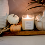 lit soy wax candle on a wooden decor board with small multicoloured decor pumpkins, candle is in the fragrance pumpkin caramel 