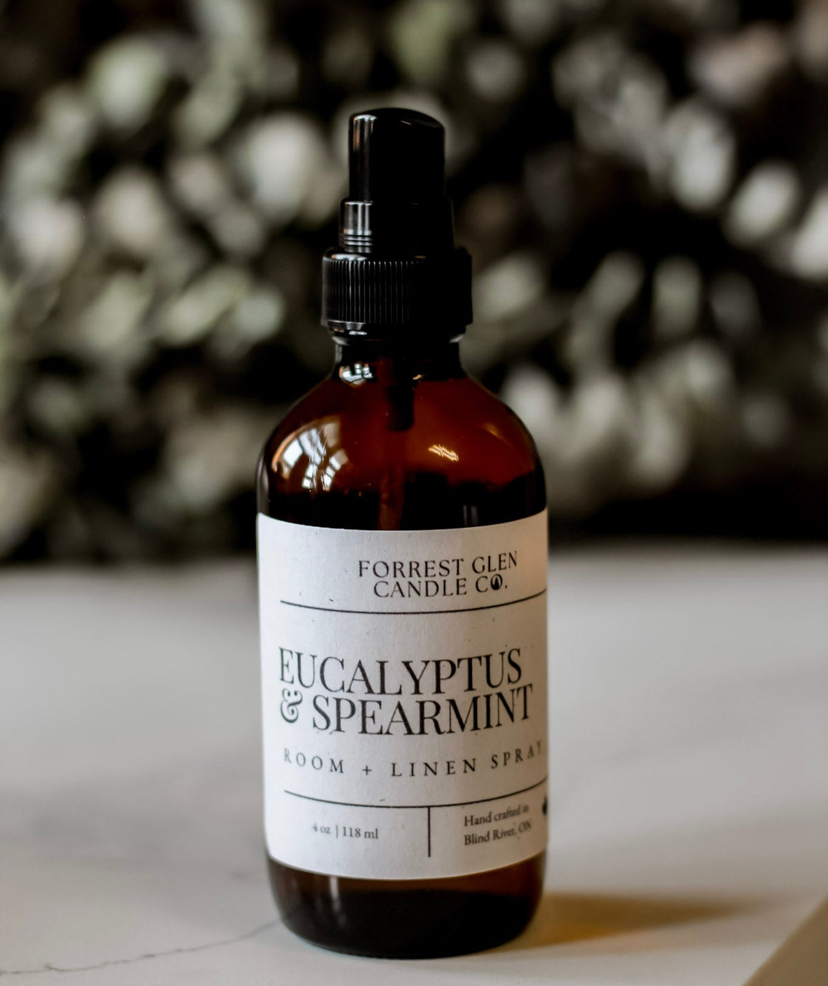 Bottle of Eucalyptus & Spearmint room and linen spray on a surface with a blurred  eucalyptus background