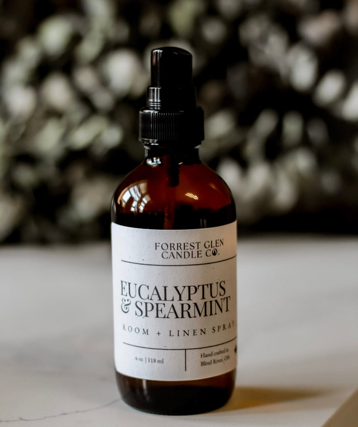 Bottle of Eucalyptus & Spearmint room and linen spray on a surface with a blurred  eucalyptus background