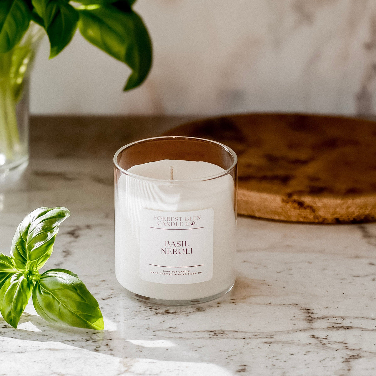 Basil Neroli candle on a marble surface with basil leaves and a plant in the background