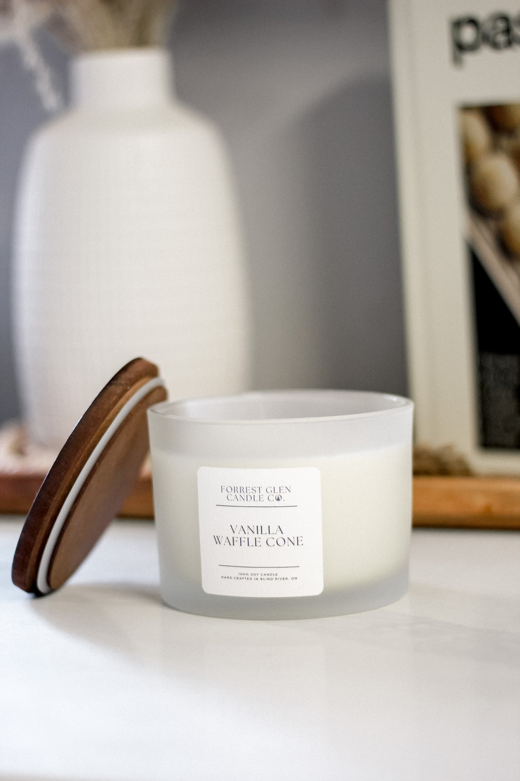 double wicked soy wax candle in a frosted glass vessel with a wooden lid in the scent vanilla waffle cone staged on a marble counter in a kitchen