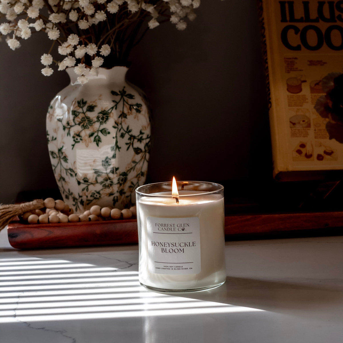 Candle labeled 'Honeysuckle Bloom' on a surface with decorative elements in the background