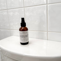 Bottle of 'Salted Caramel Macadamia' body wash on a white bathtub ledge with tiled wall background