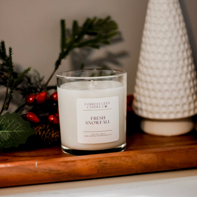 Candle labeled 'Fresh Snowfall' on a wooden surface with decorative christmas elements.