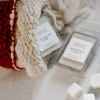 Two wax melts labeled 'Warm Winter Cabin' and 'Peppermint Vanilla' on a textured surface with a Christmas stocking