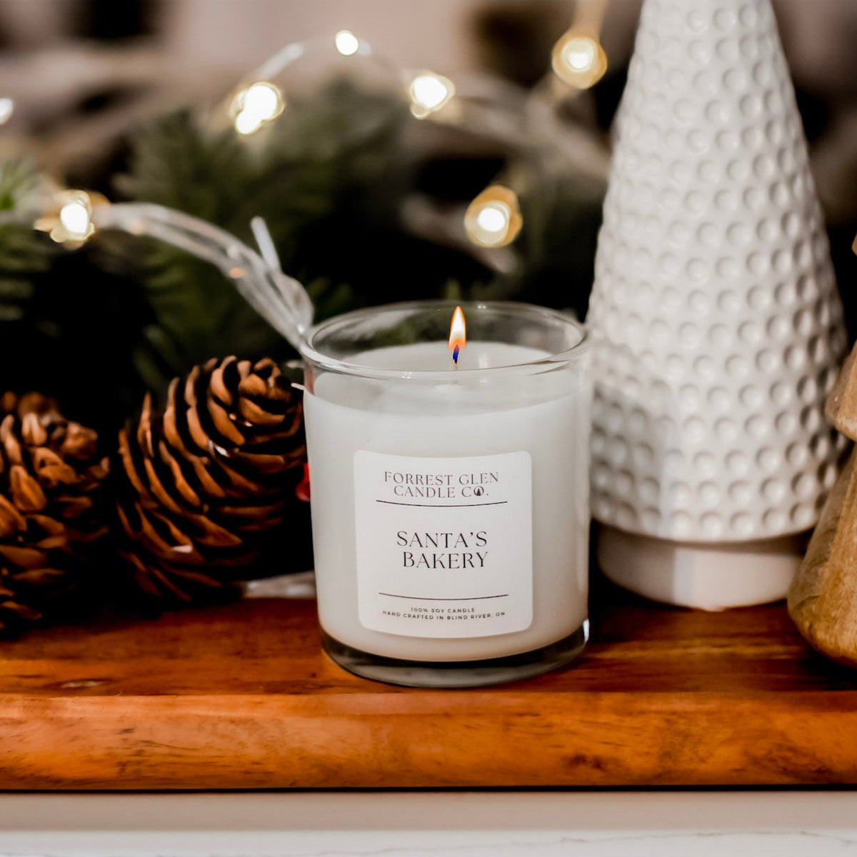 Candle labeled 'Santa's Bakery' on a wooden tray with decorative elements.