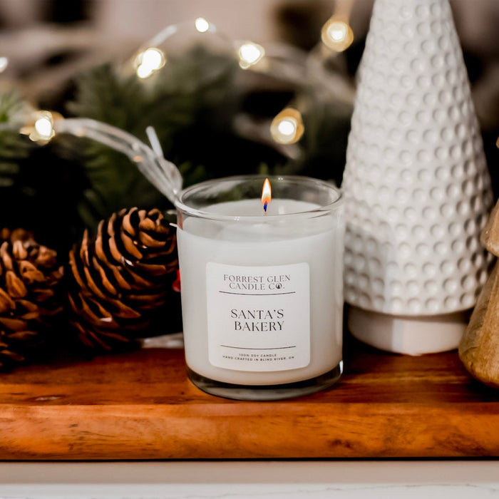 Candle labeled 'Santa's Bakery' on a wooden tray with decorative elements.