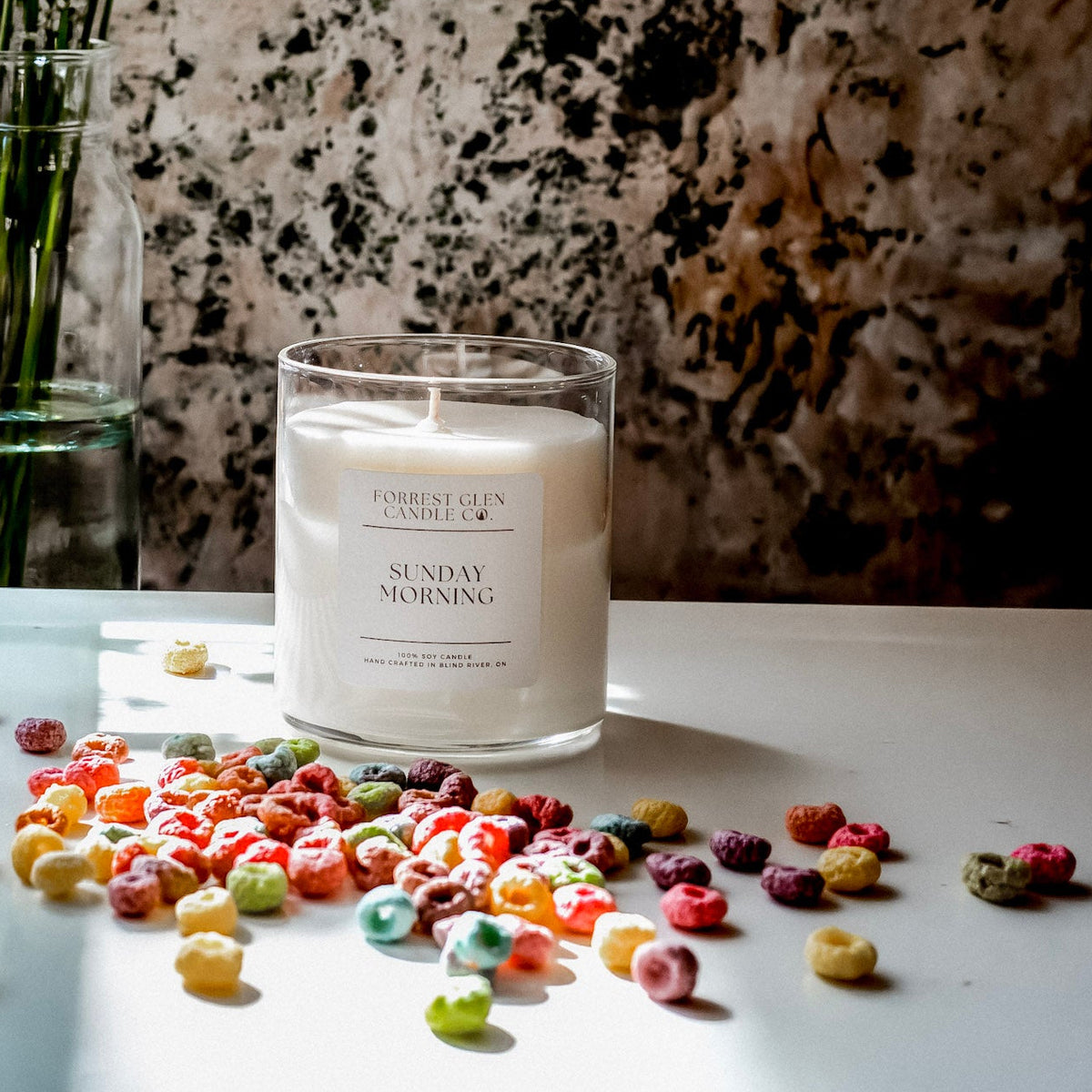Candle labeled 'Sunday Morning' on a table with colourful froot loops cereal and 
