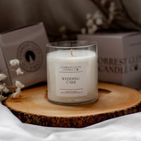 Candle labeled 'Wedding Cake' by Forrest Glen on a wooden coaster with a blurred background.