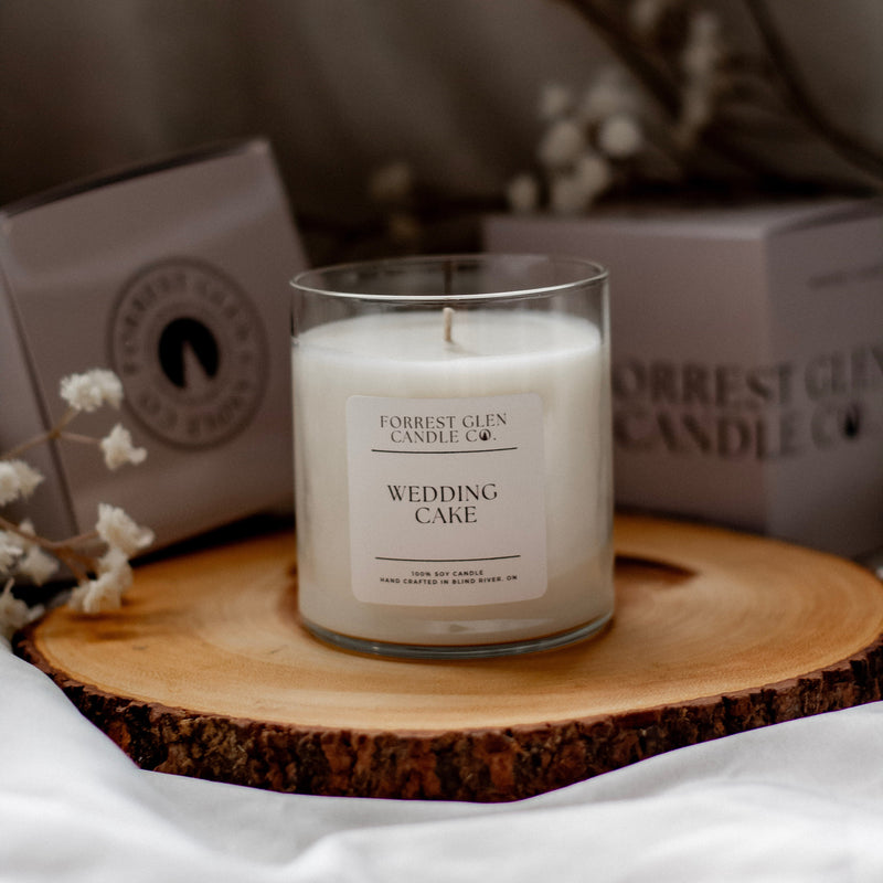 Candle labeled 'Wedding Cake' by Forrest Glen on a wooden coaster with a blurred background.