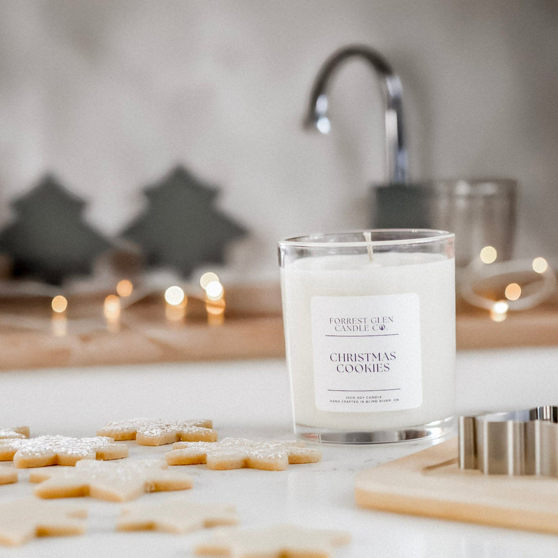 Soy wax candle labeled 'Christmas Cookies' on a kitchen counter with cookie cutters and star-shaped cookies.